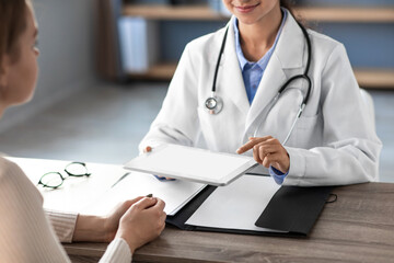 Cheerful young Hindu female doctor in white coat explains exam results from tablet to patient in office clinic. The scene highlights a friendly medical consultation atmosphere.