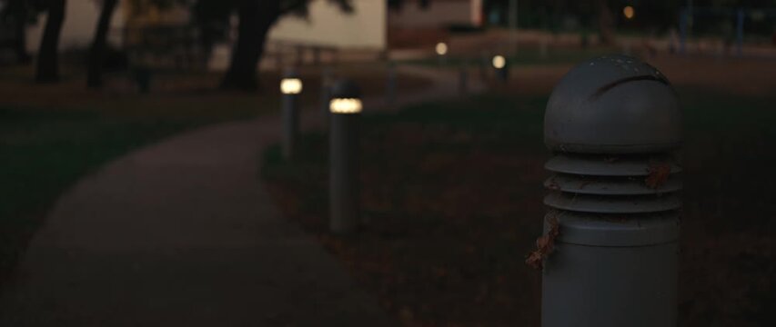 Illuminated lamps along the park pathway at sunset