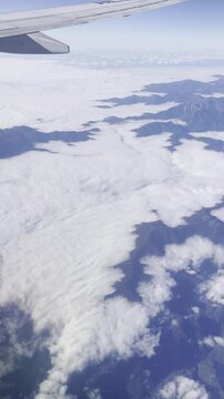 View from airplane window flying over Japan &ndash; clouds and mountain landscape under clear blue sky
