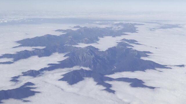 View from airplane window flying over Japan &ndash; clouds and mountain landscape under clear blue sky
