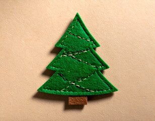 Handmade green felt Christmas tree applique with embroidered garland, flat lay on a kraft paper background with gentle shadow