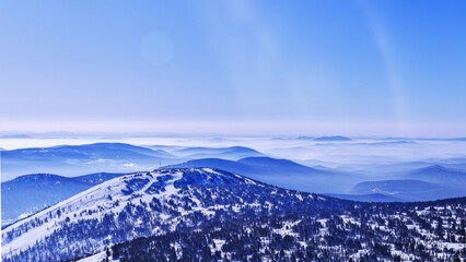 View from mount peak Mystag on Green mount, Altai mountains covered snow forest in soft blue haze, nature banner. Peaks fades in distance under clear winter blue sky, natural gradient tones.