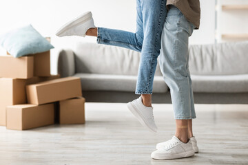 Joyful couple enjoys moving day by embracing and lifting each other in their new apartment, surrounded by moving boxes. They are excited to start this new chapter together.