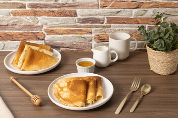 Delicious golden crepes served with honey and sauce on a rustic wooden table in a cozy setting