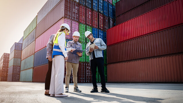 A group of workers are standing in front of a large stack of containers, looking at a clipboard