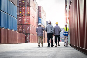 Four men in hard hats walk down a long hallway in a warehouse. They are wearing reflective vests and are likely workers in a shipping or logistics company