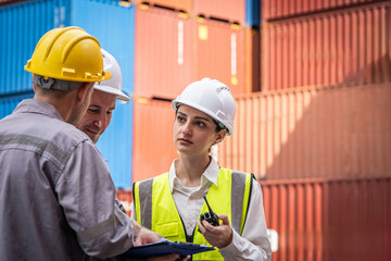 Three people are standing in front of a large container. One of them is wearing a yellow helmet