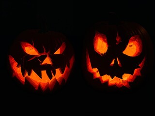 Fototapeta premium Two spooky carved Halloween pumpkins. Glowing jack-o'-lanterns with evil faces isolated on a black background.