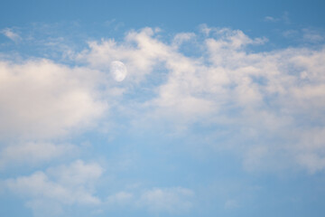 Blue sky with the moon behind white clouds