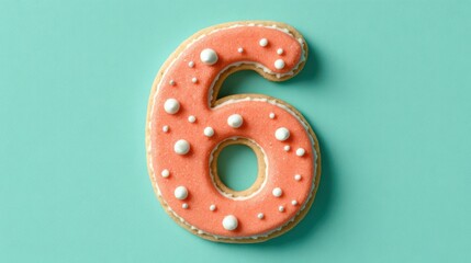 Number 6 cookie with coral frosting and white dots on a pastel turquoise background
