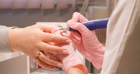Hand manicure. Fingernails care. Female beautician in gloves carefully preparing clients nail plate for procedure using electric drill in salon.