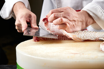On a white cutting board, the chef demonstrates his exquisite knife skills in cutting and slicing sashimi and fresh fish.
