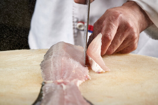 On a white cutting board, the chef demonstrates his exquisite knife skills in cutting and slicing sashimi and fresh fish.