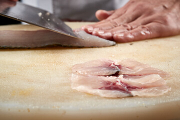 On a white cutting board, the chef demonstrates his exquisite knife skills in cutting and slicing sashimi and fresh fish.