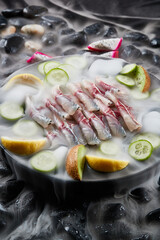 Arrange the glistening, white slices of fresh fish on a black round porcelain plate.