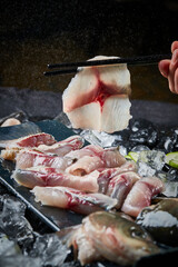 Arrange the glistening, white slices of fresh fish on a black round porcelain plate.