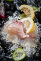 Arrange the glistening, white slices of fresh fish on a black round porcelain plate.