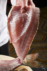 On a white cutting board, the chef demonstrates his exquisite knife skills in cutting and slicing sashimi and fresh fish.