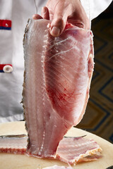 On a white cutting board, the chef demonstrates his exquisite knife skills in cutting and slicing sashimi and fresh fish.