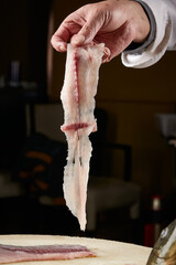 On a white cutting board, the chef demonstrates his exquisite knife skills in cutting and slicing sashimi and fresh fish.