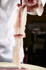 On a white cutting board, the chef demonstrates his exquisite knife skills in cutting and slicing sashimi and fresh fish.