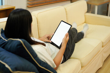 Mockup image of a woman holding black tablet pc with blank desktop white screen while lying on a...