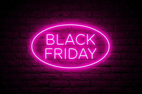 Vibrant pink neon sign displaying the words black friday glowing brightly against a dark brick wall background for seasonal sales and promotions