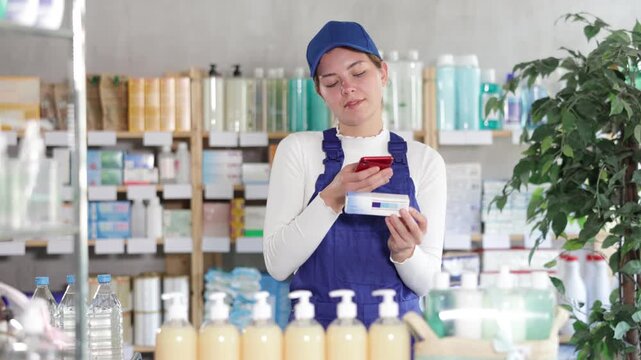 Young woman worker in uniform scanning qr code for box of ointment in pharmacy