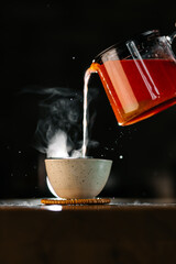 Steam rising from cup as hot tea is poured from glass teapot close-up