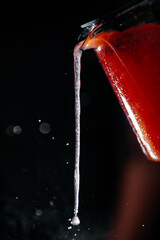 Macro shot of tea pouring from glass teapot with visible steam and droplets