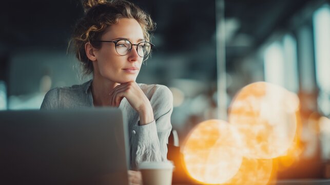 Woman in glasses sitting in her desk in the office, pensive and thinking in her - Powered by Adobe
