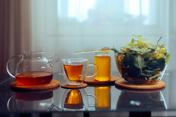Teapot and Teacup Next to a Bowl of Linden Flowers and a Honey Jar. The process of making homemade remedies from plants

