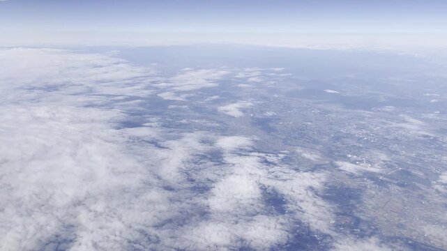 View from airplane window flying over Japan &ndash; clouds and mountain landscape under clear blue sky
