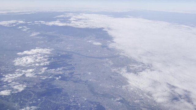 View from airplane window flying over Japan &ndash; clouds and mountain landscape under clear blue sky

