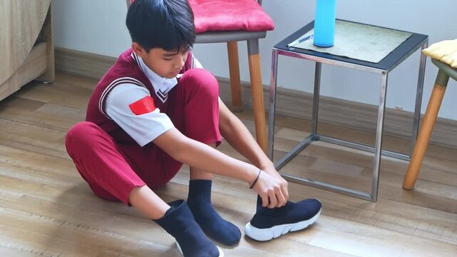 Young asian student dressed in uniform carefully puts on shoes before school day begins