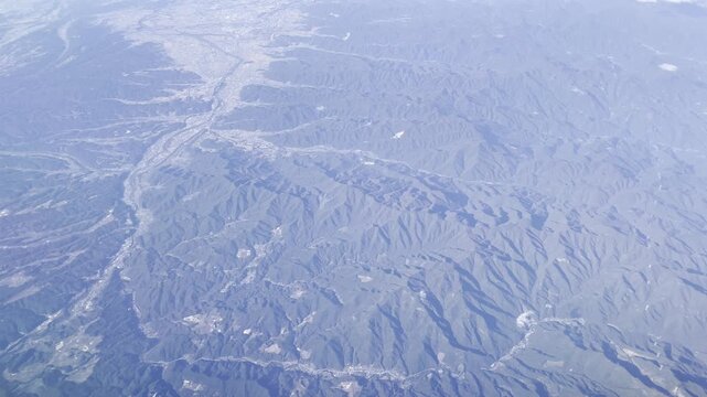 View from airplane window flying over Japan &ndash; clouds and mountain landscape under clear blue sky
