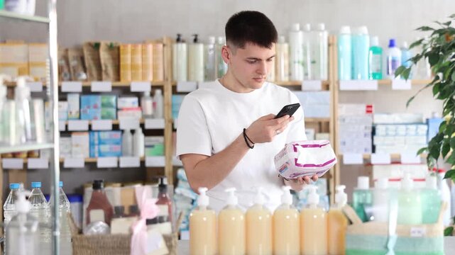 Guy scans the barcode of a package of pads in a pharmacy. Young man takes a photo on mobile camera and sends a photo of pads to his wife to clarify which ones to buy. High quality 4k footage