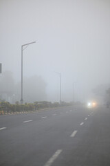 Cars drive through dense fog on a misty morning road