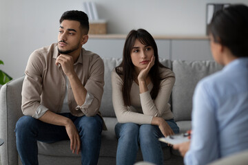 Two offended Arab spouses sit apart on a couch during marital therapy, clearly avoiding eye contact...