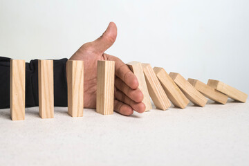 male hand stop falling wooden blocks. domino effect or risk protection strategy concept