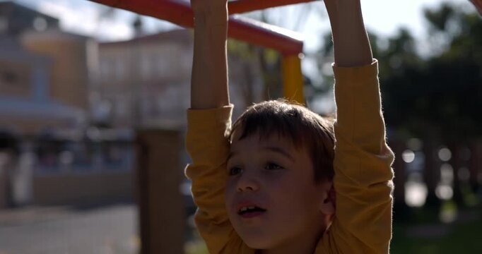 Young boy holding onto monkey bars at park - tilt up shot