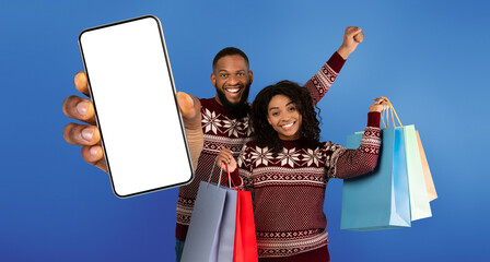 Ready for New Year celebration. Happy african american couple holding many colorful shopping bags and smiling to camera over blue studio background