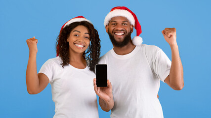 Yes. Excited black couple holding smartphones with empty screen shaking clenched fists, celebrating...