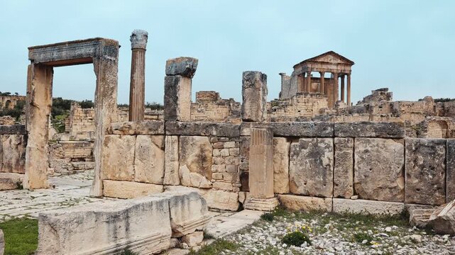 Scenic view of remnants of ancient Roman settlement of Dougga overlooking historic gate of Dar Lacheb and Capitol Temple ruins in backdrop under cloudy spring sky, Tunisia