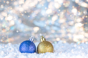 Glittery blue and gold Christmas ornament resting in snow with soft bokeh lights