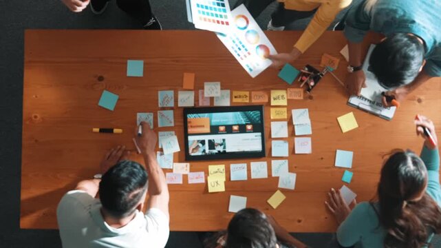 Top view of business people working together to design web design. Aerial view of designer brainstorming and discussing about website interface and looking at tablet with digital design. Symposium.