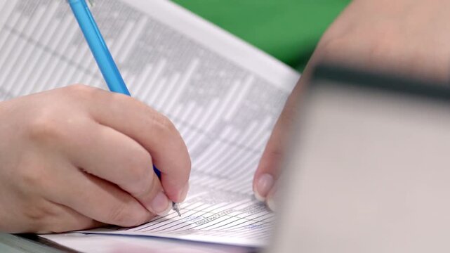 Close-up of a hand writing data on paper forms with a blue pen. Office paperwork, record keeping, business administration, accuracy, documentation, and organization in a modern workplace