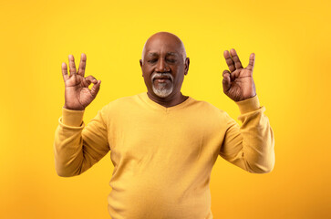 Elderly African American man meditates with closed eyes, seeking calm and inner balance. The bright orange background enhances the peaceful atmosphere of his stress relief practice.