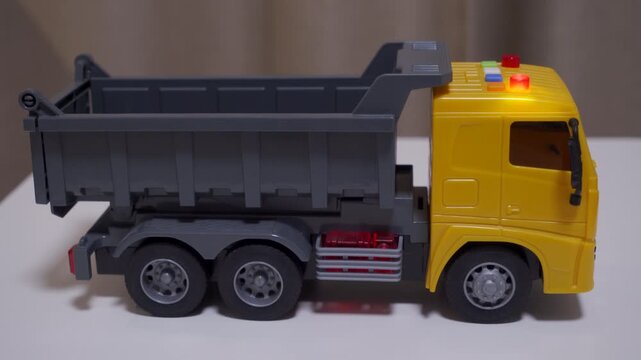 A yellow and gray plastic toy dump truck flashes its roof lights. It makes a beeping sound, like it is reversing.