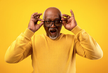 A senior African American man wearing glasses expresses surprise and excitement about a huge sale or discount. His joyful reaction highlights the unbelievable offer against an orange studio backdrop.